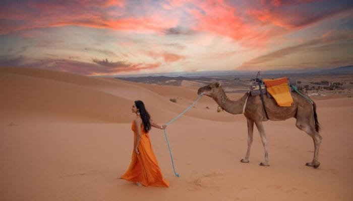 a woman walking with a camel in the desert