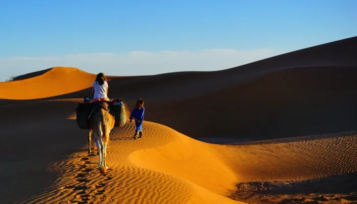 a woman and child riding a camel in the desert